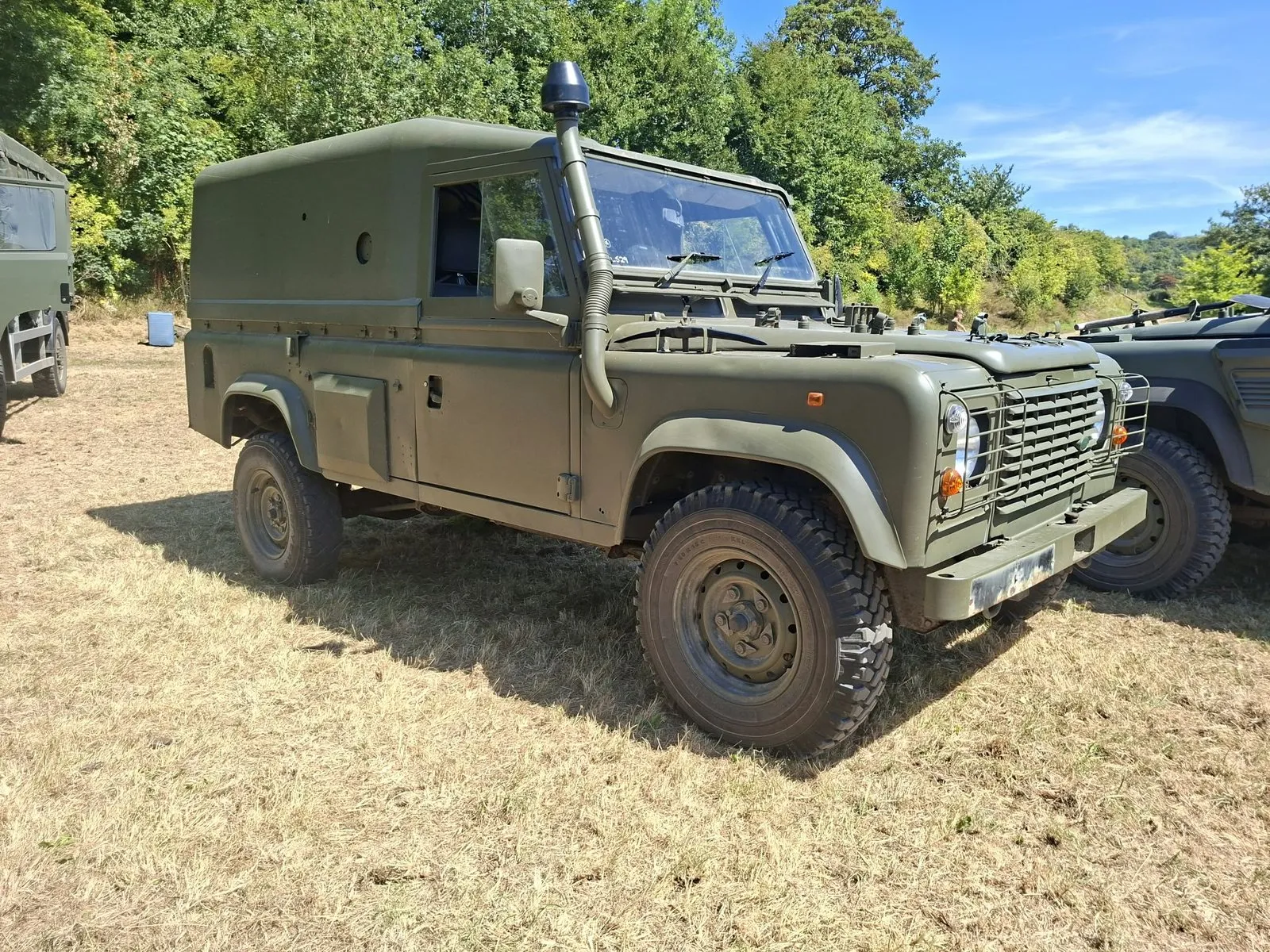 NATO green Land Rover Defender Wolf 110 hardtop with a snorkel, parked on dry grass